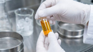 Mains gantées tenant une fiole contenant un extrait liquide doré dans un laboratoire scientifique.